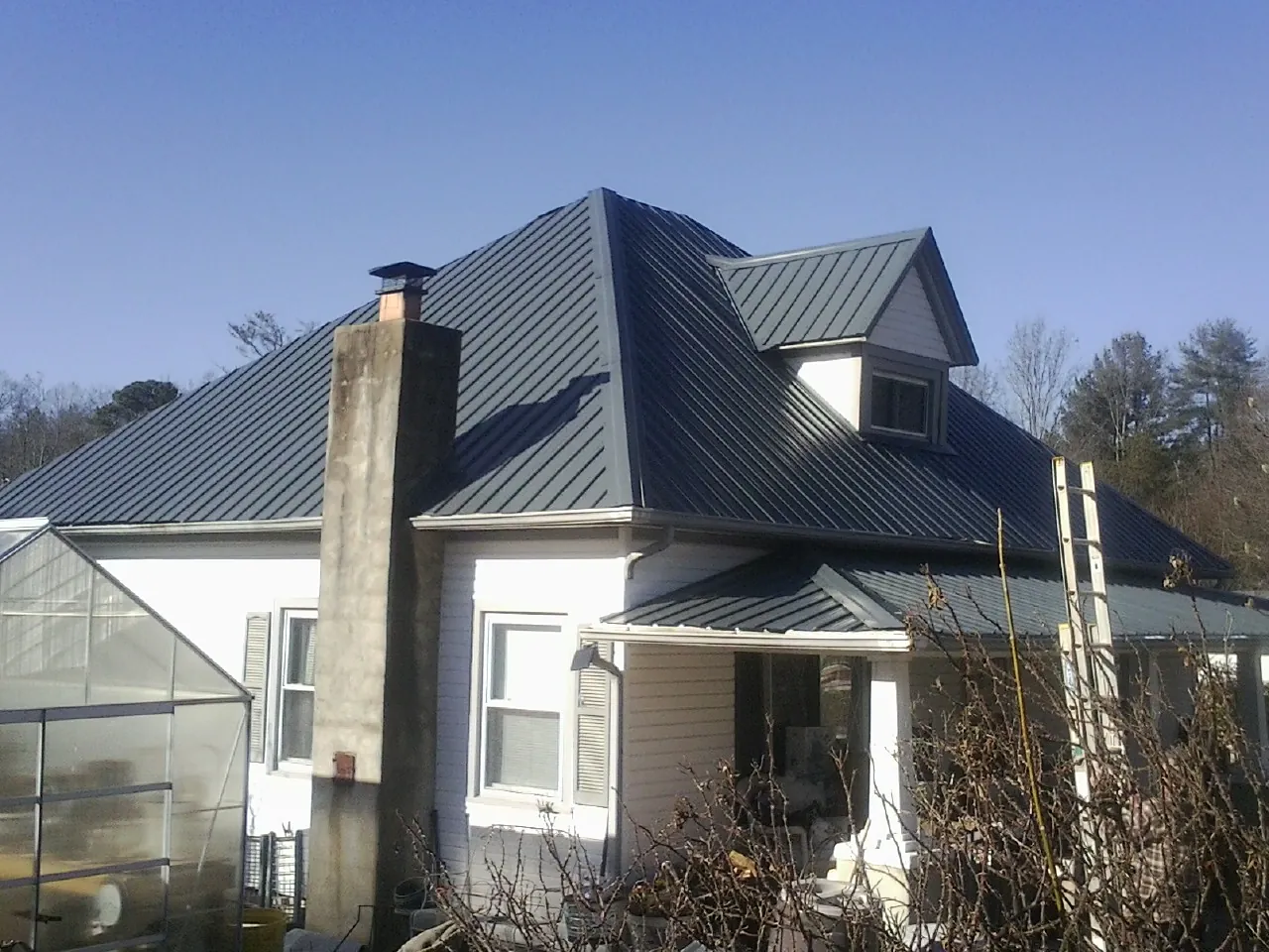 Dark blue standing seam metal roof on a white farmhouse with dormer — Slate & Tile Roof Repair by Roofing Brothers in Moody
