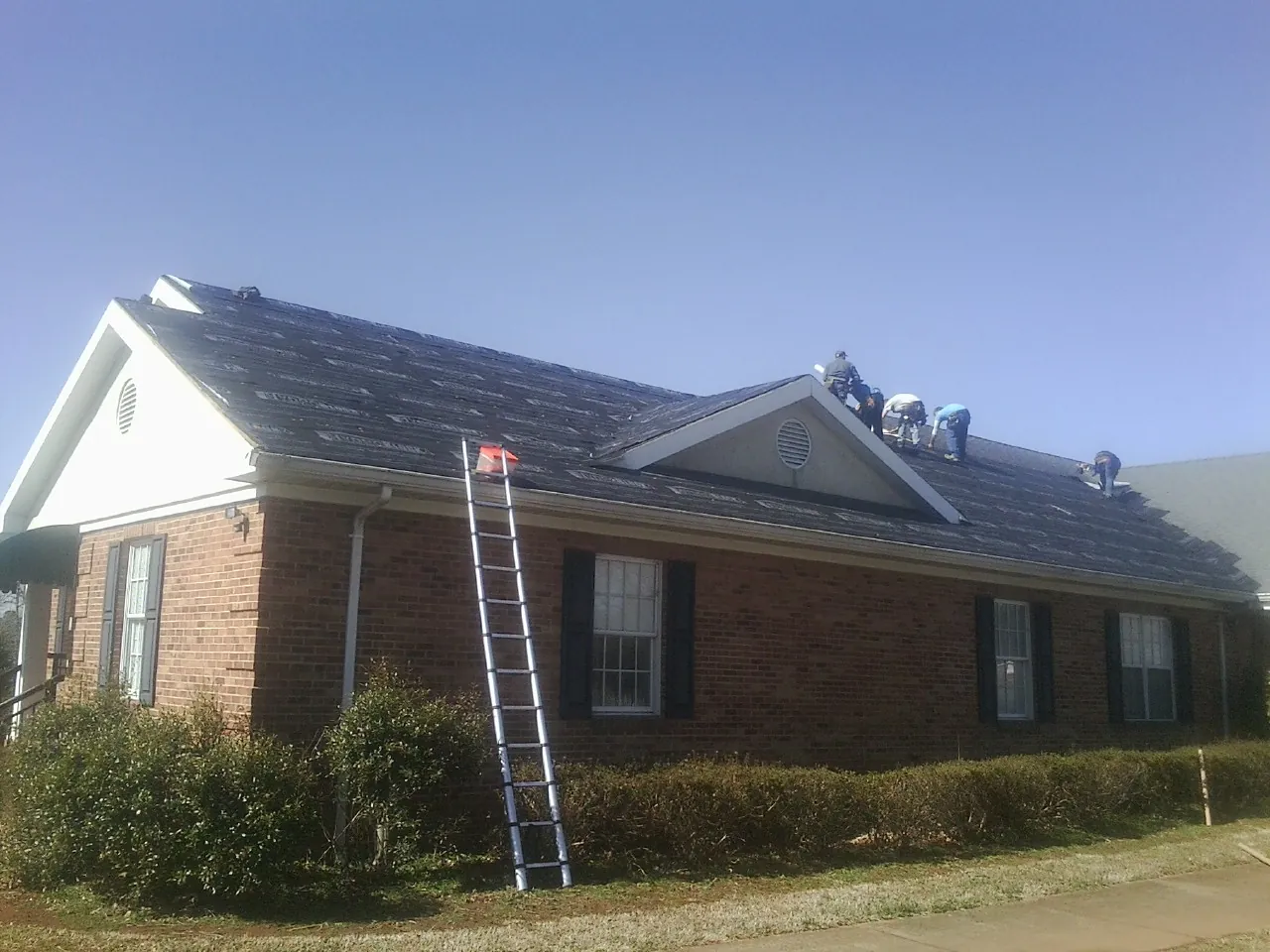 Crew tearing shingles off a brick ranch roof with a ladder set — Emergency Roof Repair work by our crew in Moody