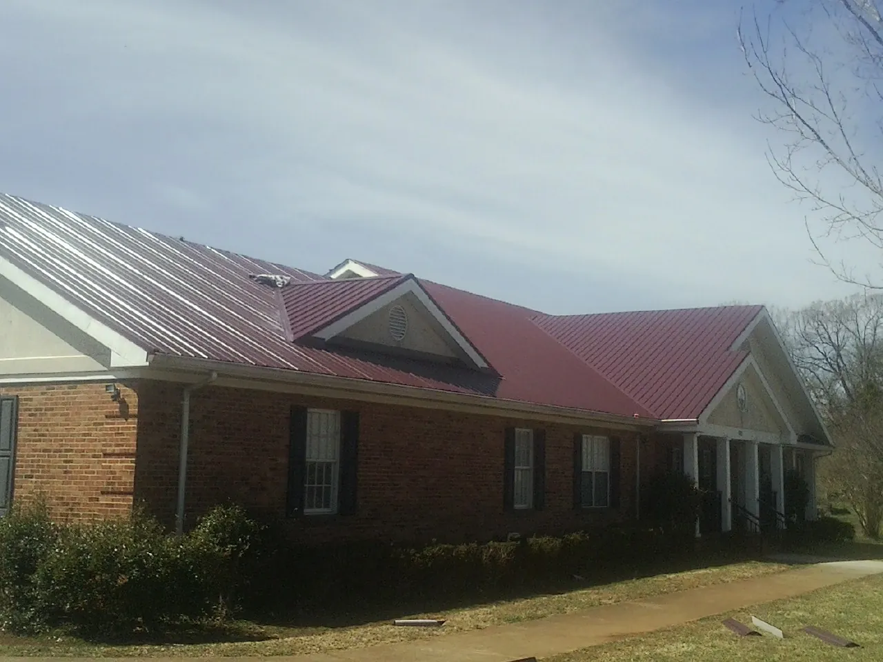 Red metal roof with gabled entries on a long brick building, from a Hail Damage Roof Repair job in Moody