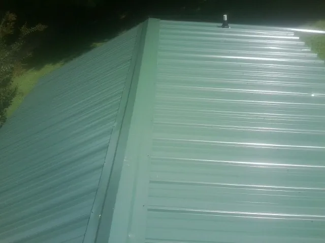 New green metal panels meeting at the ridge of a roof — Flat Roof Repair work by our crew in Moody