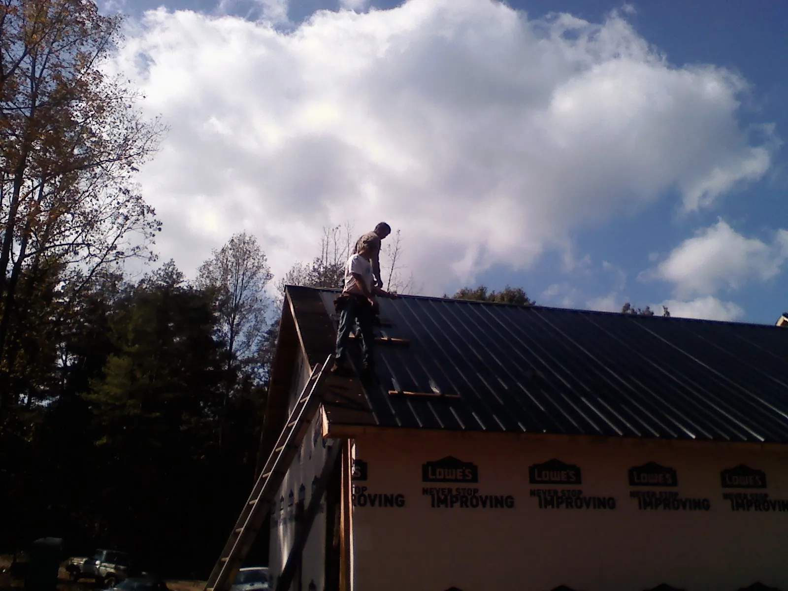 Roofer fastening dark metal panels high against a cloudy sky, from a Roof Inspection job in Moody